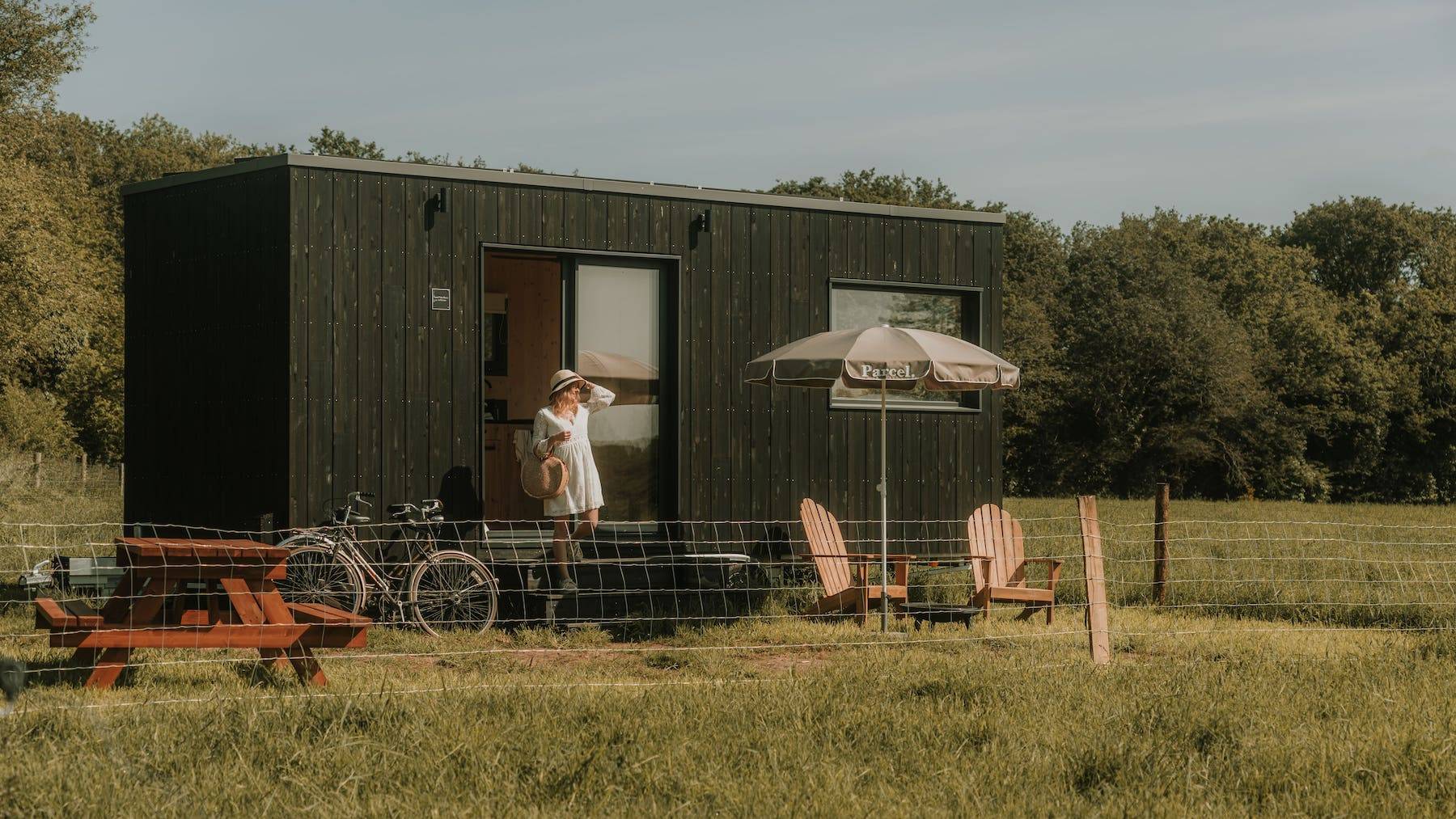 Mujer saliendo de Tiny House con sombrero y bolso