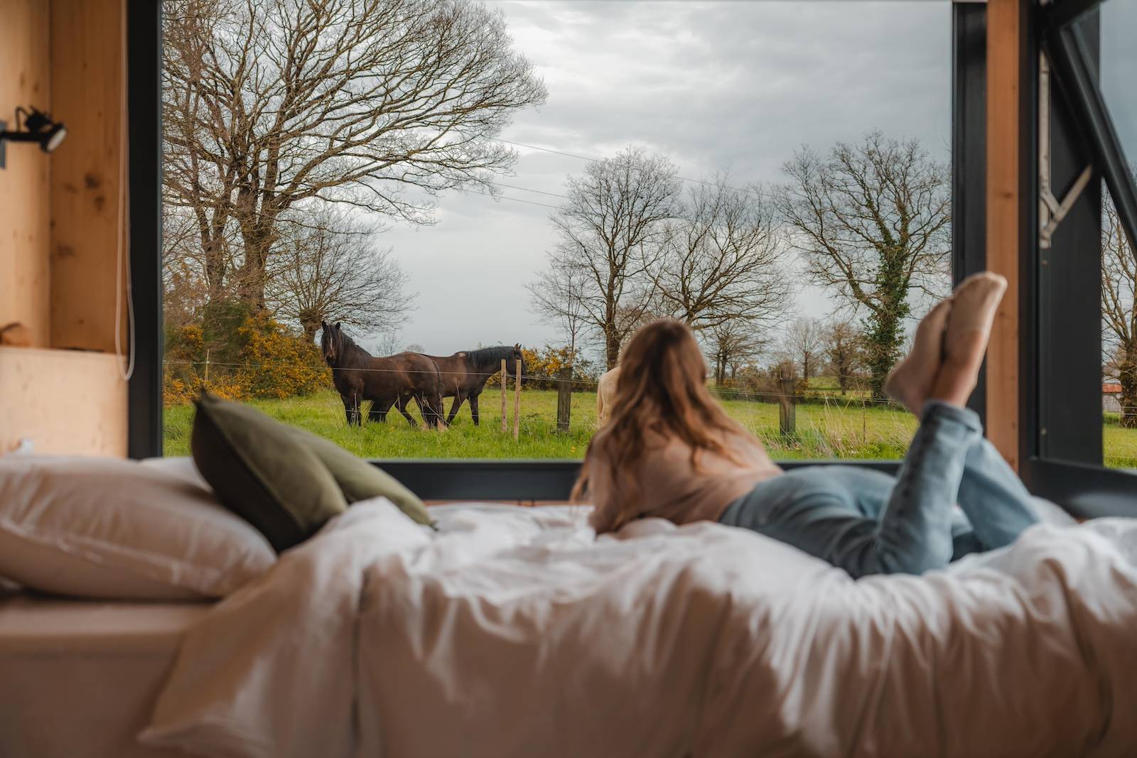 Une femme regarde les chevaux par la fenêtre de sa tiny house