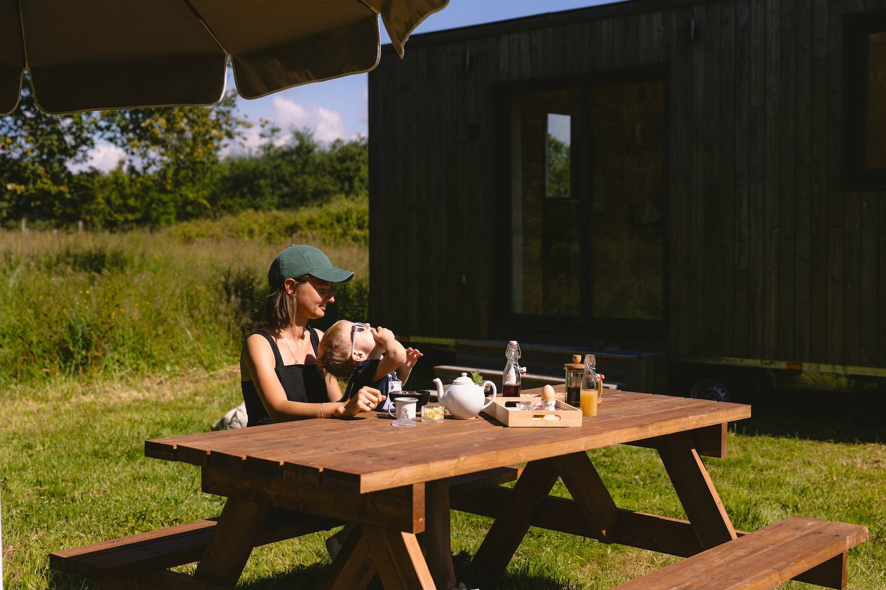 Un enfant et sa maman déjeune sur une table en bois devant la Tiny House