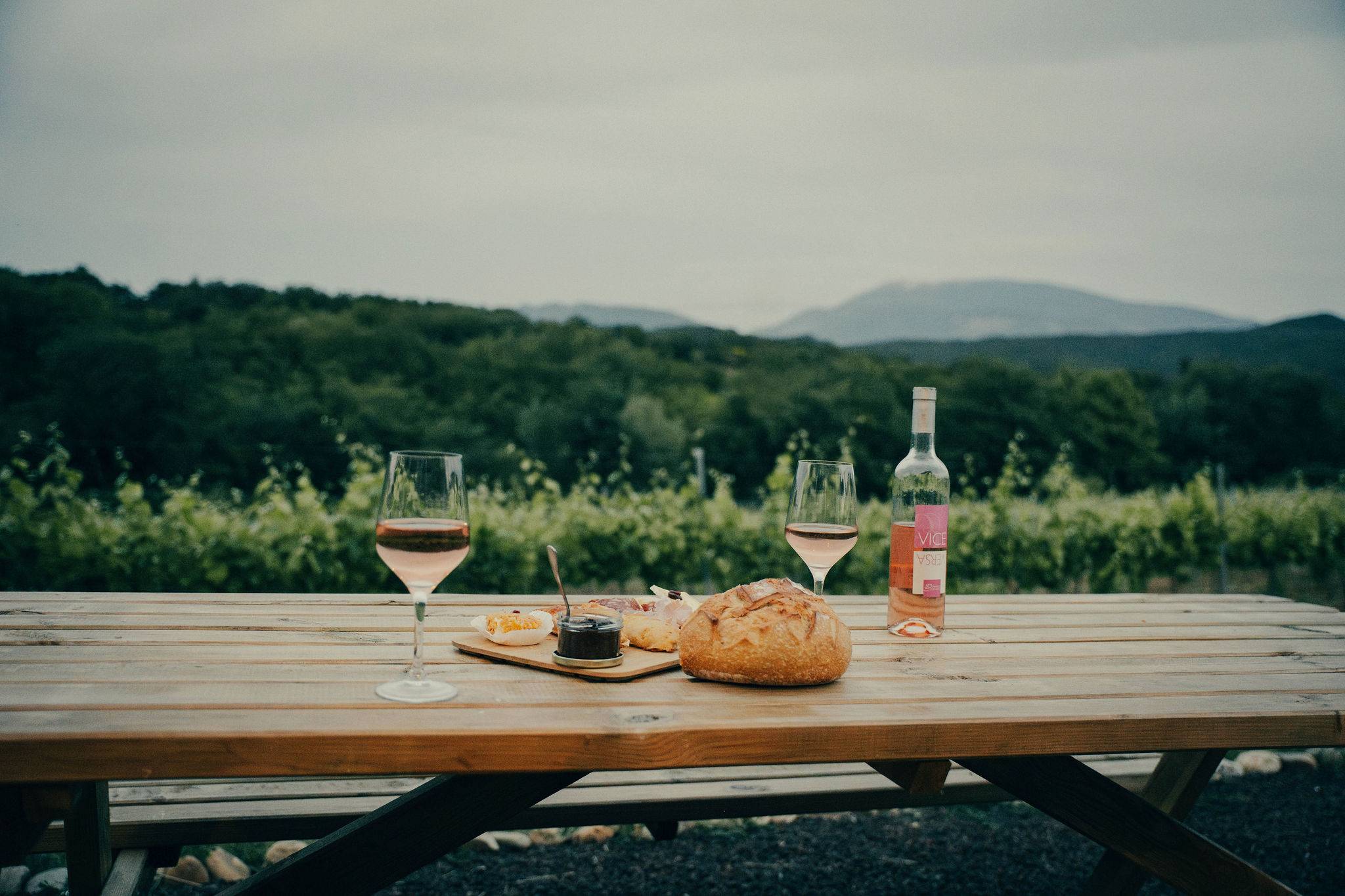prise de vue d'une table en bois face à la montagne avec une bouteille de vin, deux verres de vins plein et une planche apéritif